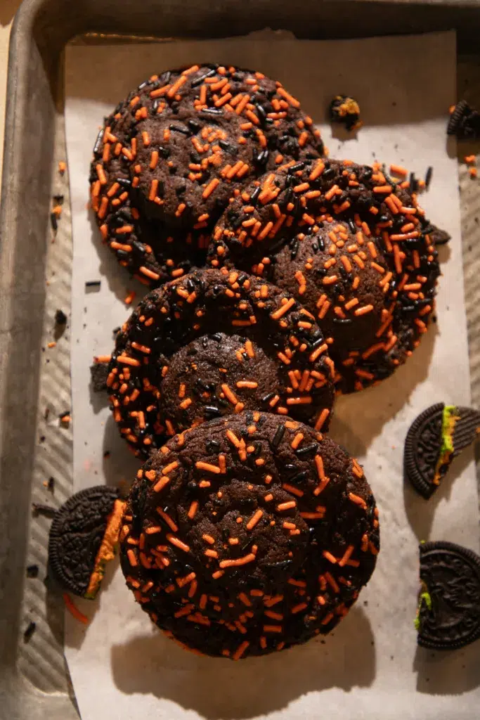 Rows of chocolate Oreo cookies decorated with black and orange sprinkles on a baking tray.