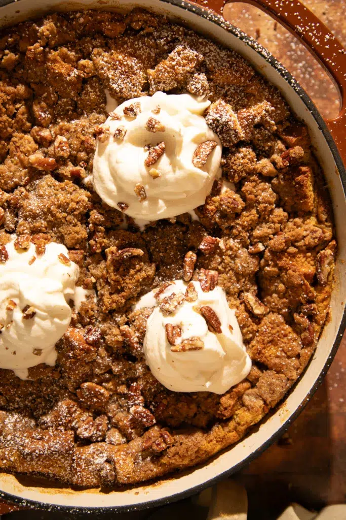 Overhead view of baked pumpkin brioche French toast casserole topped with pecan streusel, whipped cream, and a dusting of powdered sugar.