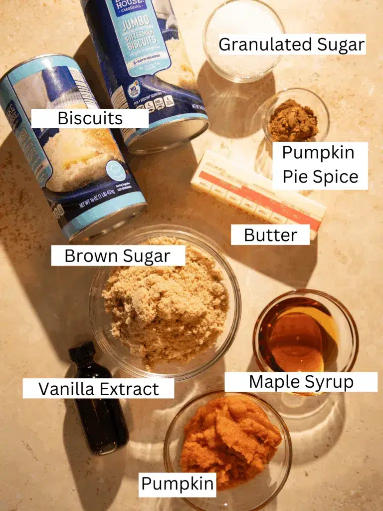 Overhead shot of ingredients for pumpkin spice monkey bread muffins, including canned biscuits, sugars, butter, pumpkin puree, pumpkin pie spice, vanilla, and maple syrup.