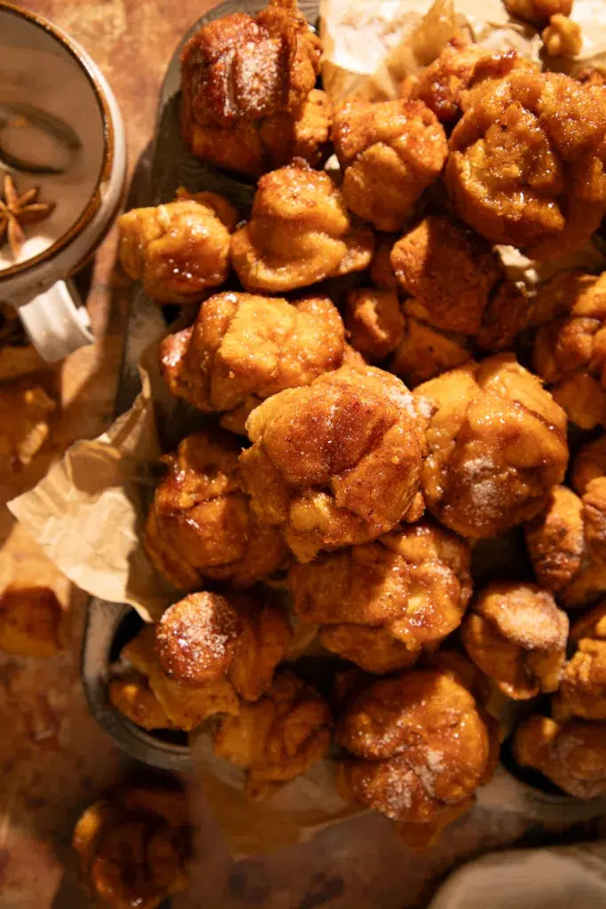 Pumpkin monkey bread muffin pulled apart to reveal fluffy layers coated in pumpkin spice caramel glaze.
