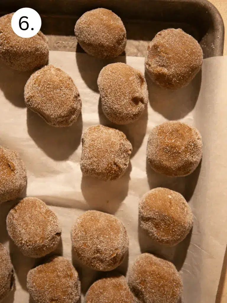 Cookie dough balls rolled in sugar and lined up on a parchment-lined baking sheet before baking.