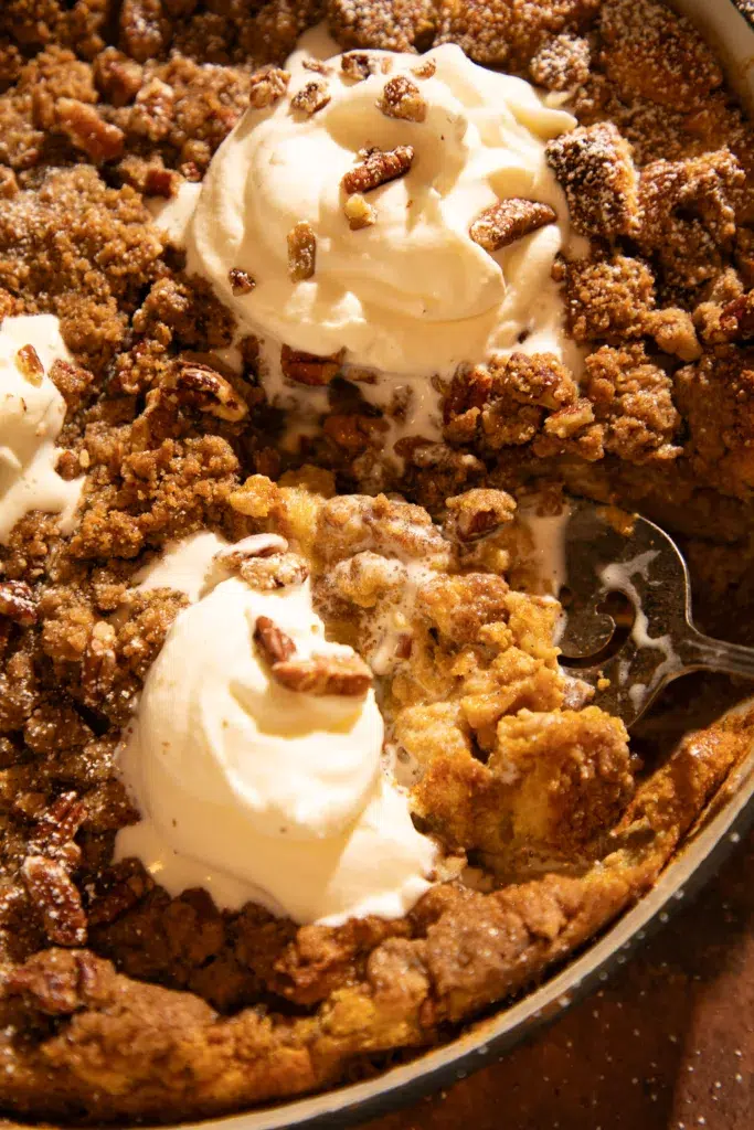 Pumpkin brioche French toast casserole in baking dish with portions scooped out, showing soft pumpkin custard inside and pecan topping.