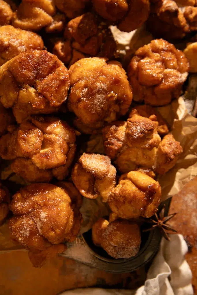 Warm-toned photo of pumpkin spice monkey bread muffins on parchment-lined tray with star anise for styling.