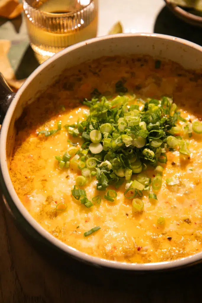Tortilla chip dipped into cheesy green chile dip with melted cheese and green onion topping.
