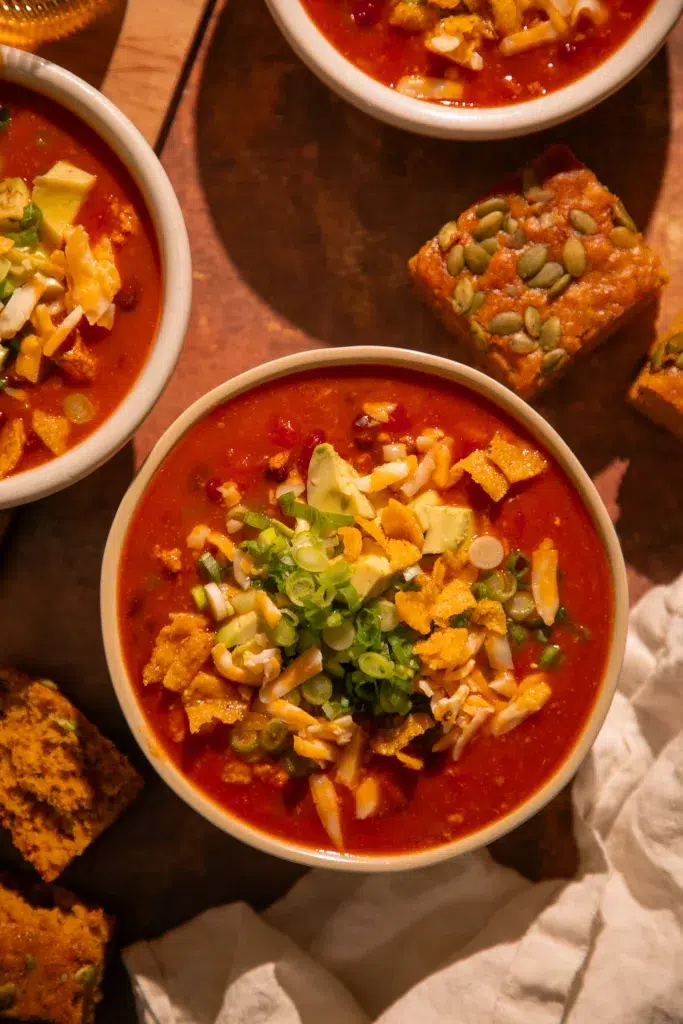 Bowl of pumpkin turkey chili with fall garnishes, surrounded by cornbread slices.