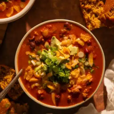 Bowl of pumpkin turkey chili with fall garnishes, surrounded by cornbread slices.