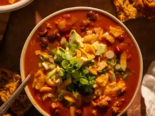 Bowl of pumpkin turkey chili with fall garnishes, surrounded by cornbread slices.