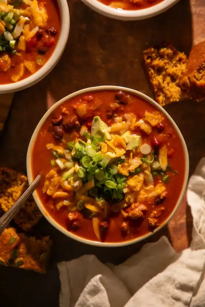 Bowl of pumpkin turkey chili with fall garnishes, surrounded by cornbread slices.