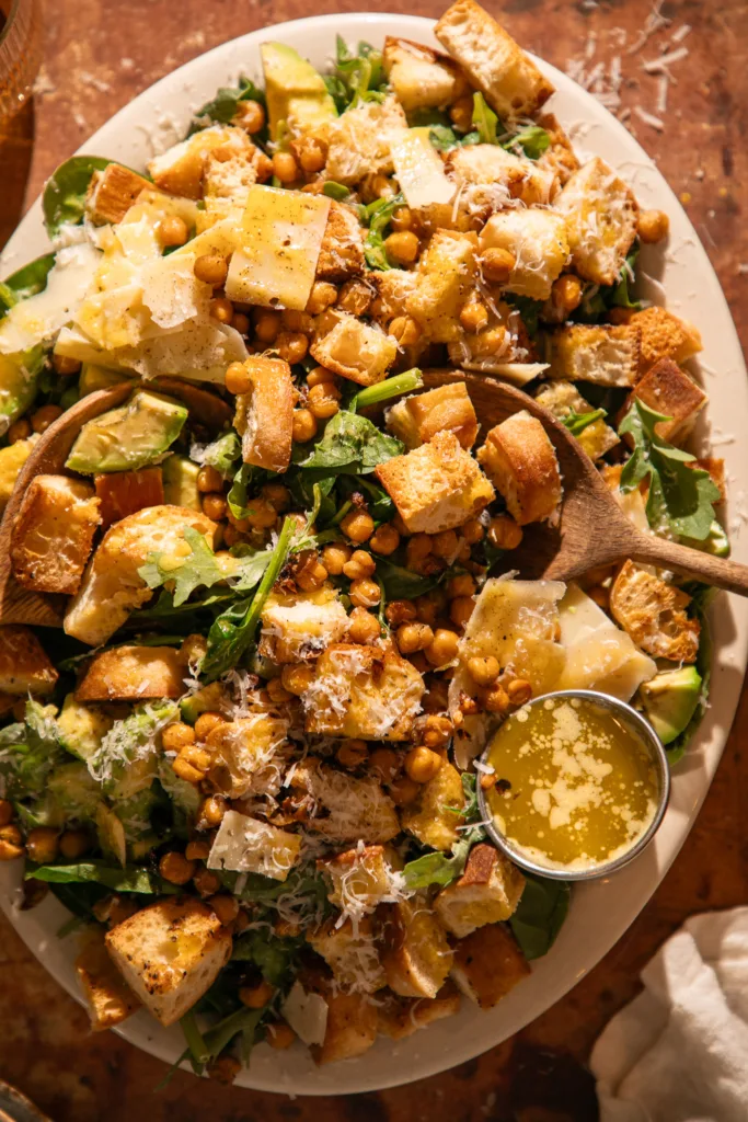 Close view of spinach Caesar salad showing crispy chickpeas, golden croutons, and fresh parmesan cheese.