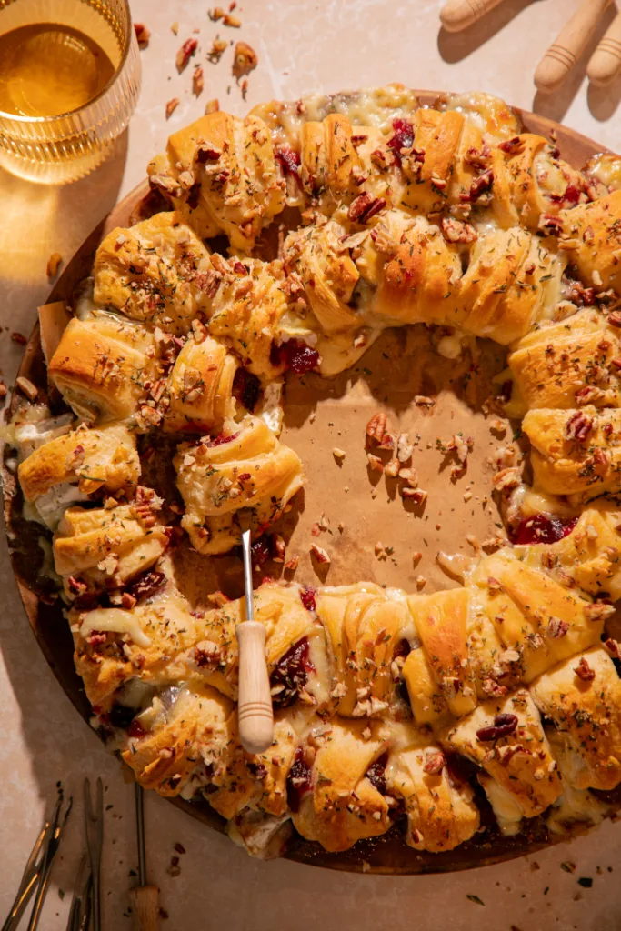 Close-up of cranberry brie crescent ring with melted brie cheese, cranberries, and toasted pecans, a piece being served with a fork.