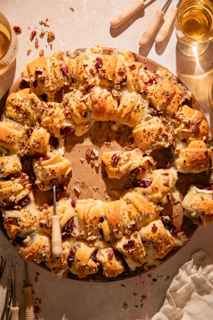 Overhead of cranberry brie crescent roll wreath baked golden brown, with melted brie and cranberry sauce oozing between layers.