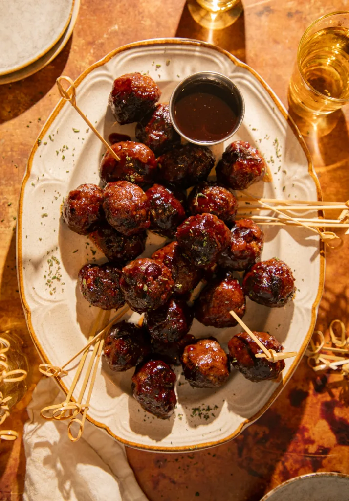 Glazed cranberry balsamic meatballs served on a ceramic platter with cocktail picks and extra sauce for dipping, styled for the holidays.
