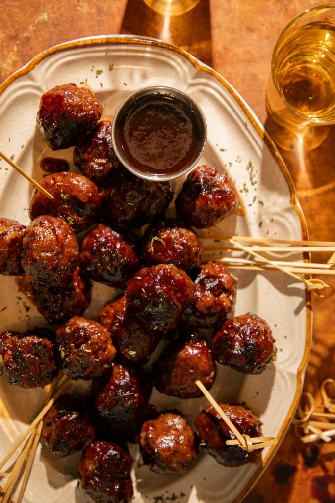 Juicy cocktail meatballs coated in glossy cranberry balsamic glaze with herbs and cocktail skewers, perfect for Thanksgiving or holiday appetizers