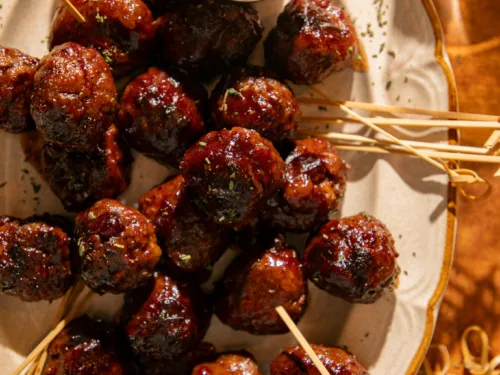 Close-up of holiday cranberry BBQ meatballs with deep caramelized glaze and festive warm lighting on a rustic platter.