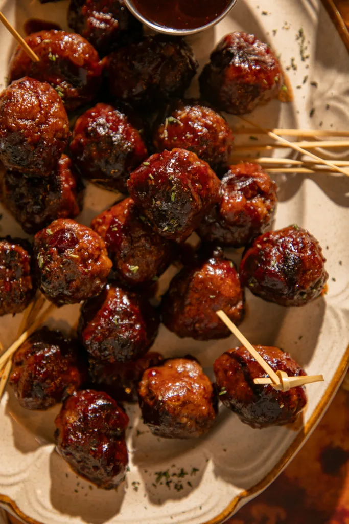 Bite-size cocktail meatballs arranged with cocktail sticks and extra dipping sauce, ideal for party spreads or holiday gatherings.