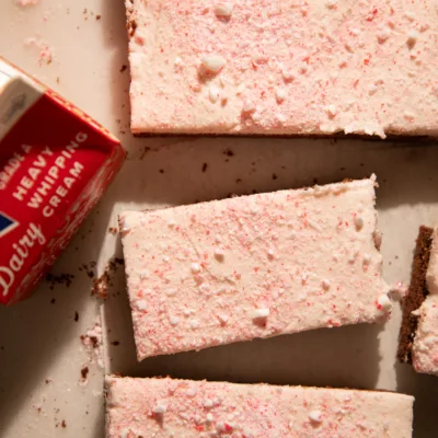 Peppermint mocha cookie bars arranged on a white surface with a carton of heavy cream for a cozy holiday look.