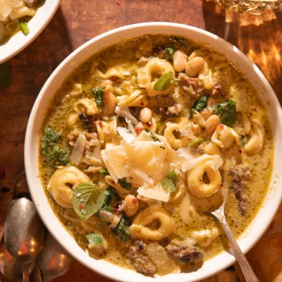 Warm bowl of slow cooker tortellini soup with sausage, spinach, pesto, and white beans, served with crusty bread.