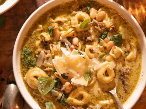 Warm bowl of slow cooker tortellini soup with sausage, spinach, pesto, and white beans, served with crusty bread.