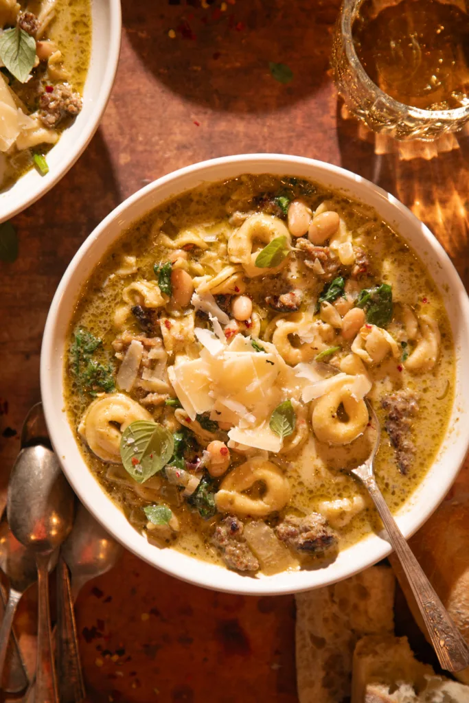 Warm bowl of slow cooker tortellini soup with sausage, spinach, pesto, and white beans, served with crusty bread.