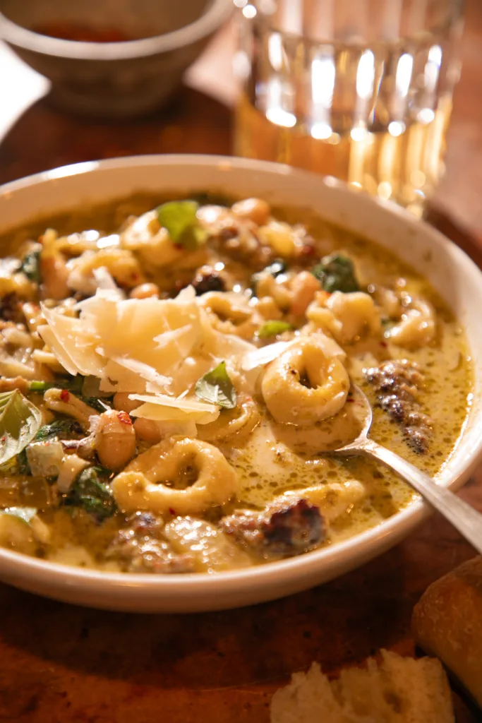 Close-up of creamy tortellini soup in a slow cooker with sausage, spinach, pesto, and melted parmesan.