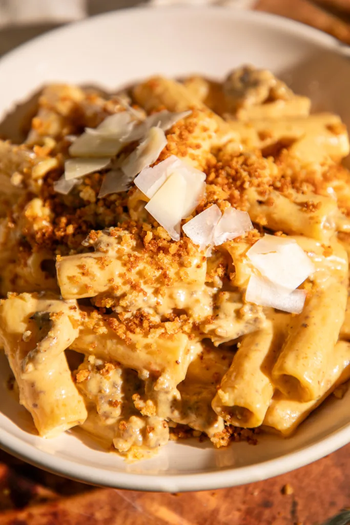 Close-up view of rigatoni coated in brown butter pumpkin Alfredo sauce with spicy sausage, breadcrumbs, and Parmesan shavings.