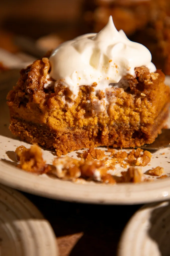 Close-up of pumpkin pie bar with a bite taken out, showing the creamy pumpkin filling and crumbly oat topping topped with whipped cream.