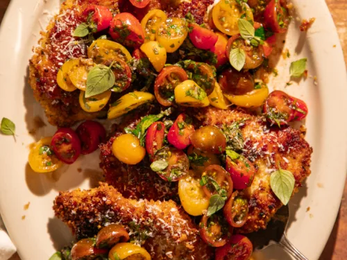 Crispy chicken cutlets topped with lemon herb tomato bruschetta made with cherry tomatoes, basil, and parsley, served on a white platter with grated Parmesan and olive oil drizzle.