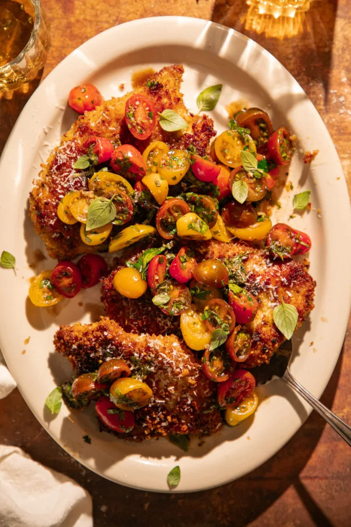 Crispy chicken cutlets topped with lemon herb tomato bruschetta made with cherry tomatoes, basil, and parsley, served on a white platter with grated Parmesan and olive oil drizzle.