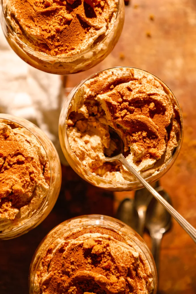 Overhead view of layered gingerbread tiramisu cups topped with cinnamon and crushed gingersnaps in glass dishes.