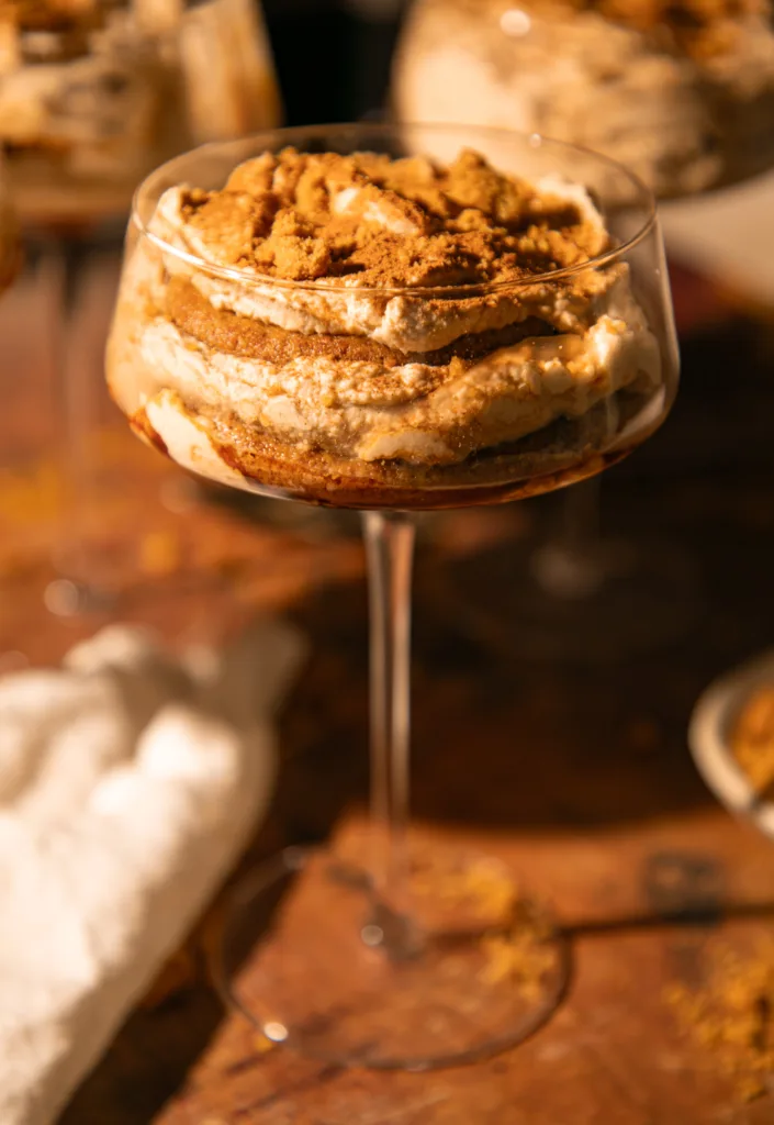 Side view of a glass filled with layers of espresso-soaked gingersnaps and creamy mascarpone filling dusted with cinnamon.