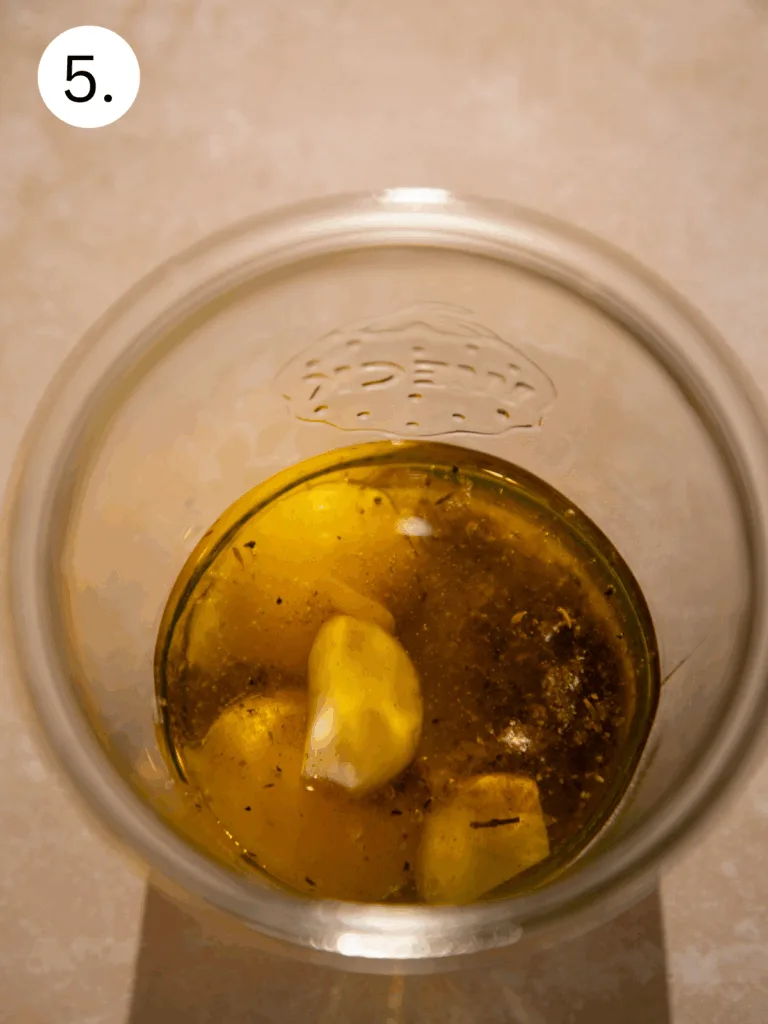 Garlic cloves and olive oil in a glass jar with seasoning, the base for homemade Caesar salad dressing.