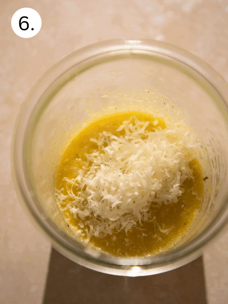 Freshly grated parmesan being added to garlic and olive oil mixture for a creamy Caesar salad dressing.