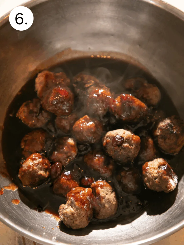 Warm baked meatballs coated in a rich cranberry balsamic BBQ sauce inside a mixing bowl, steaming and ready to serve.