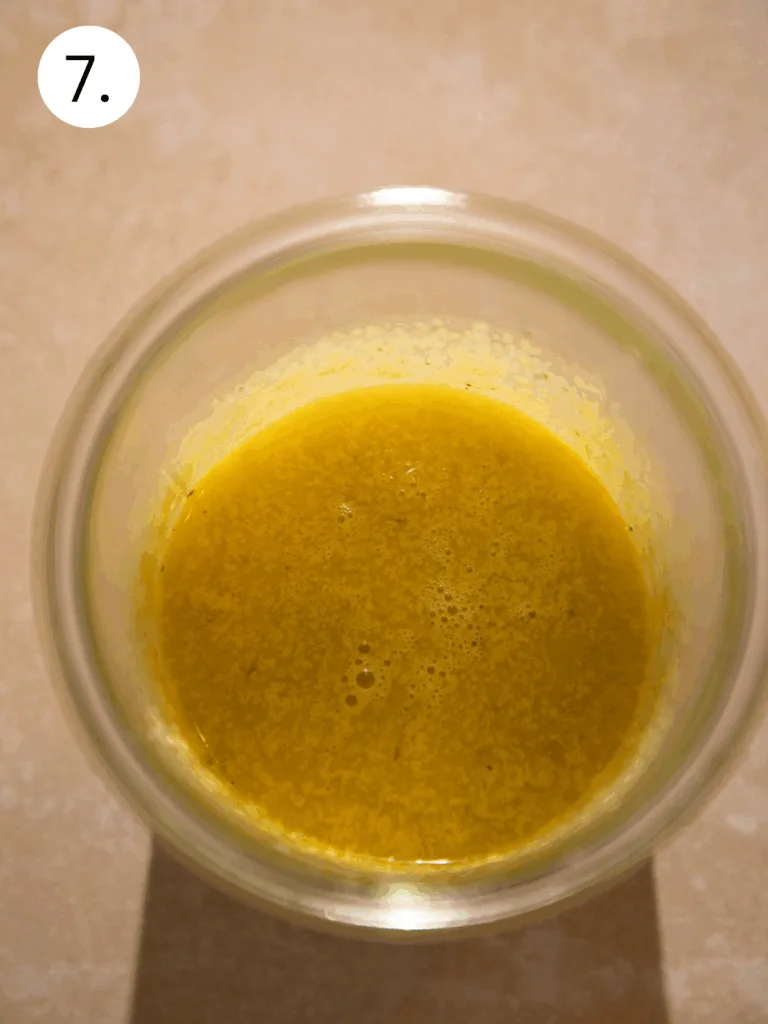 Smooth golden Caesar dressing mixture in a glass jar after blending olive oil, garlic, and parmesan.