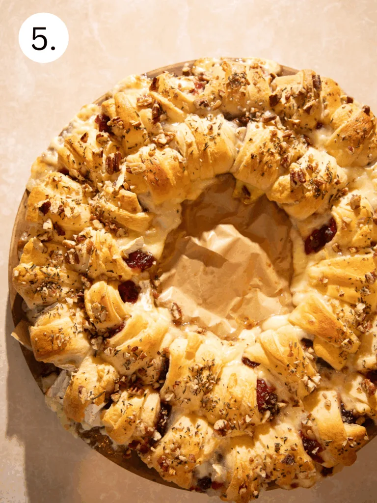 Overhead view of baked cranberry brie crescent ring with melted brie, cranberries, pecans, and rosemary.