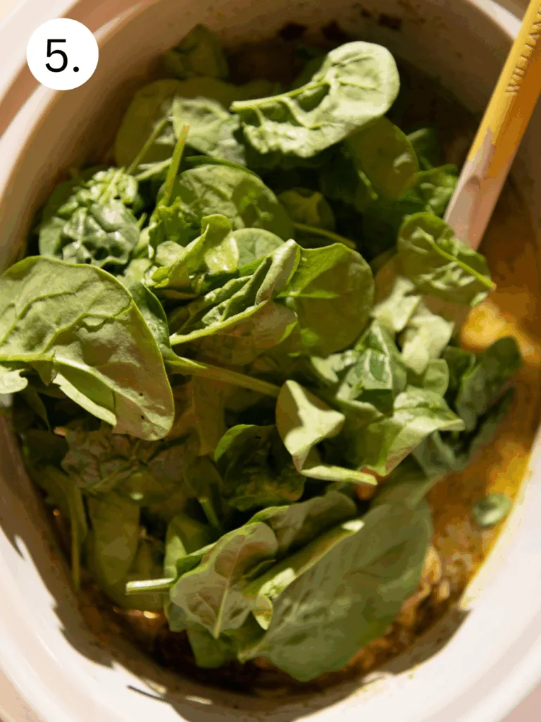 Fresh spinach leaves added to a slow cooker filled with creamy pesto broth and sausage for white tortellini soup.