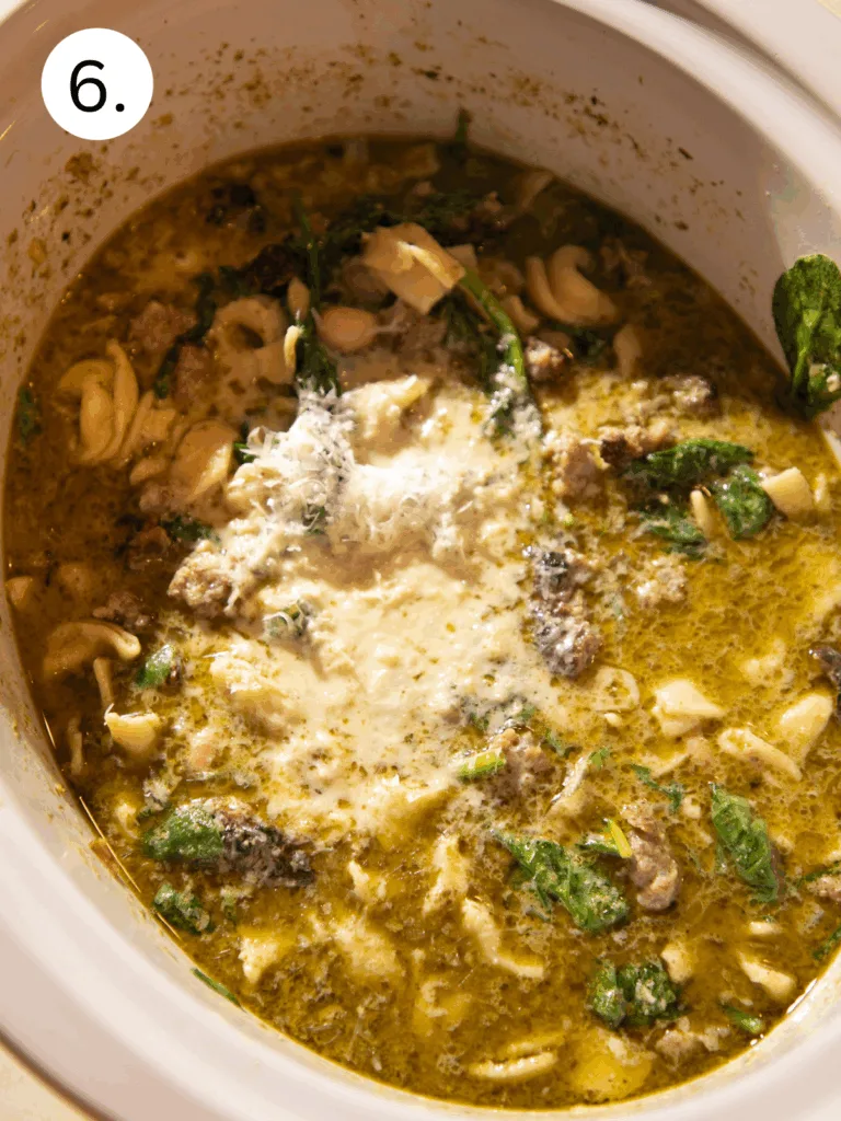Warm bowl of slow cooker tortellini soup with sausage, spinach, pesto, and white beans, served with crusty bread.