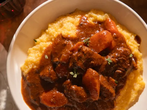 Close-up bowl of Instant Pot red wine braised beef tips served over creamy polenta, topped with fresh thyme and surrounded by warm lighting.