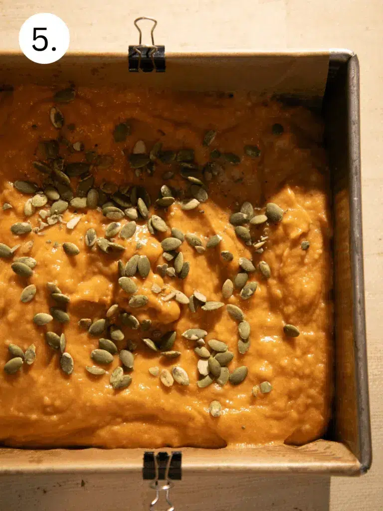 Pumpkin banana bread batter in a loaf pan topped with pepitas, ready to bake.
