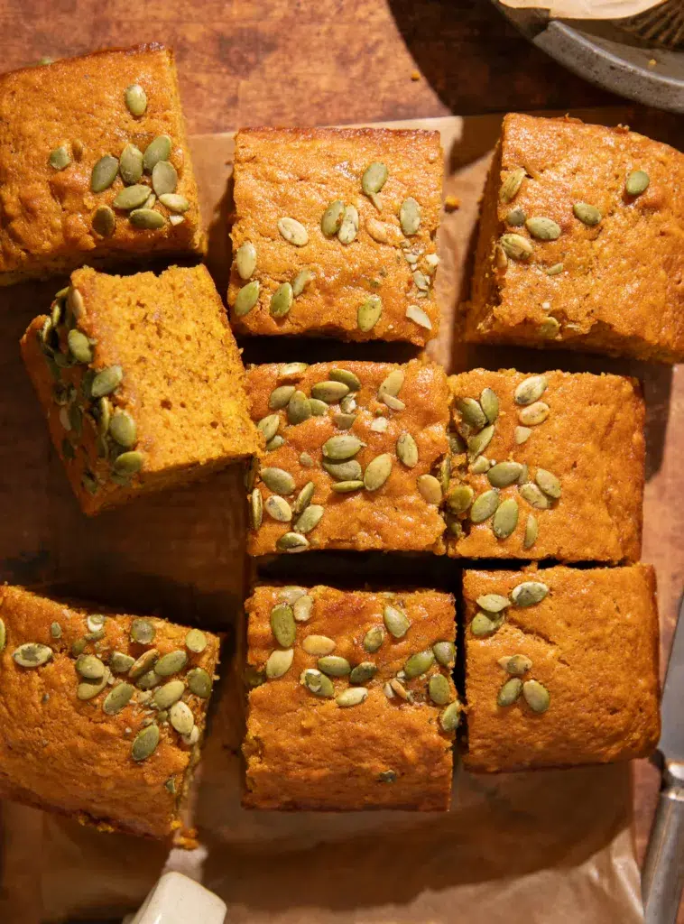 Golden pumpkin banana bread squares sprinkled with pepitas on a parchment-lined surface.