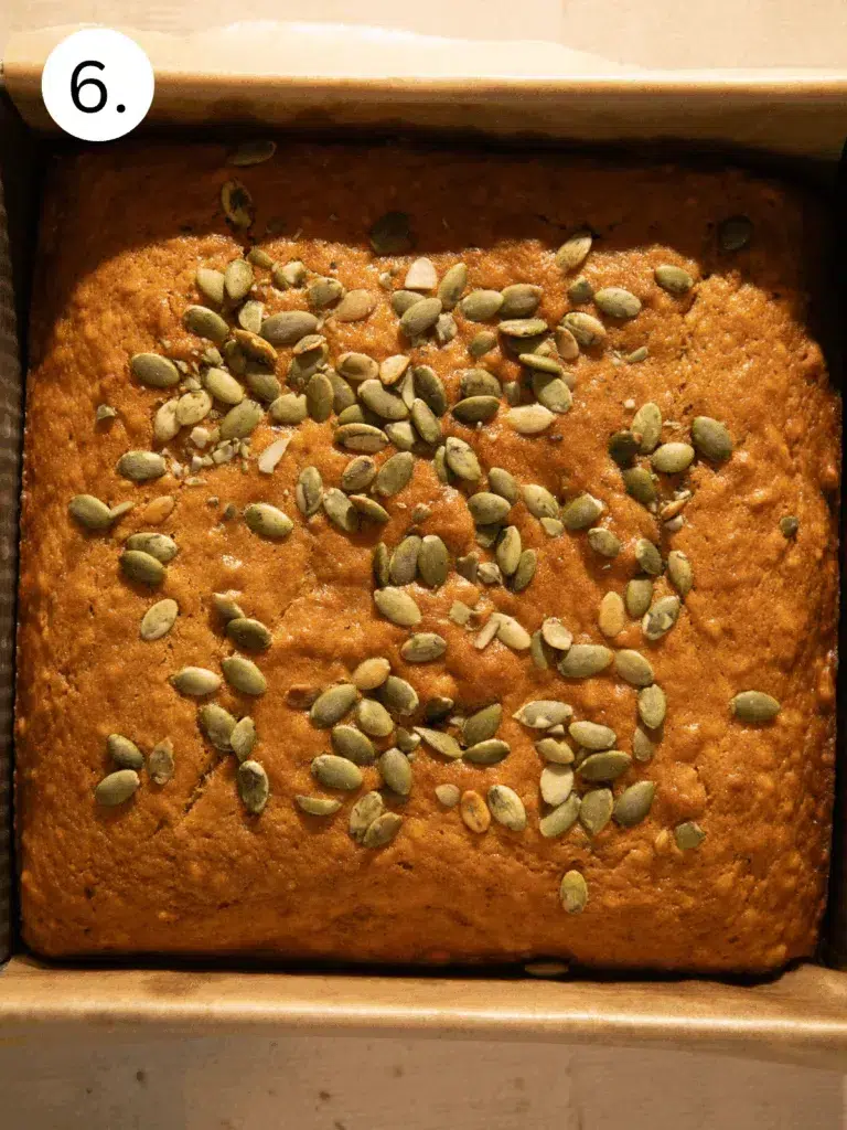 Moist maple pumpkin banana bread cut into squares and topped with crunchy pepitas on parchment paper.