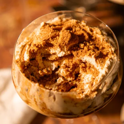 Close-up of no-bake gingerbread tiramisu topped with crushed gingersnaps and cinnamon in a clear dessert glass.
