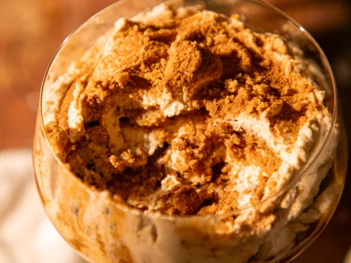 Close-up of no-bake gingerbread tiramisu topped with crushed gingersnaps and cinnamon in a clear dessert glass.