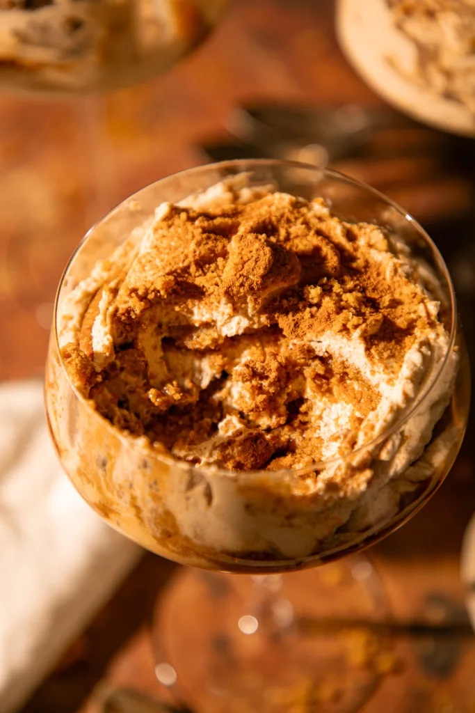 Close-up of no-bake gingerbread tiramisu topped with crushed gingersnaps and cinnamon in a clear dessert glass.
