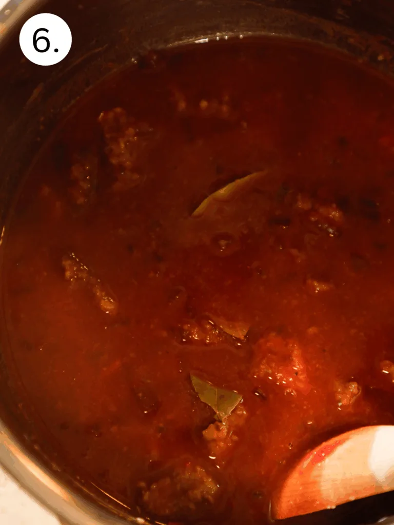 Thick red wine sauce simmering in the Instant Pot with bay leaves and tender beef tips visible