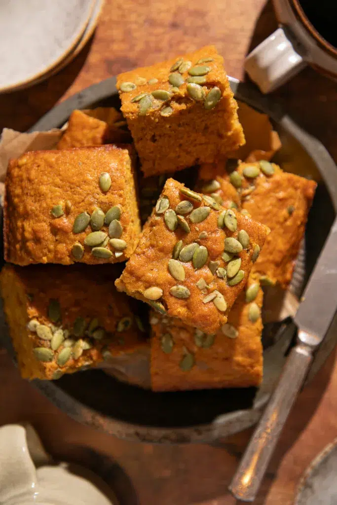 Rustic serving dish filled with squares of maple pumpkin banana bread topped with pepitas.