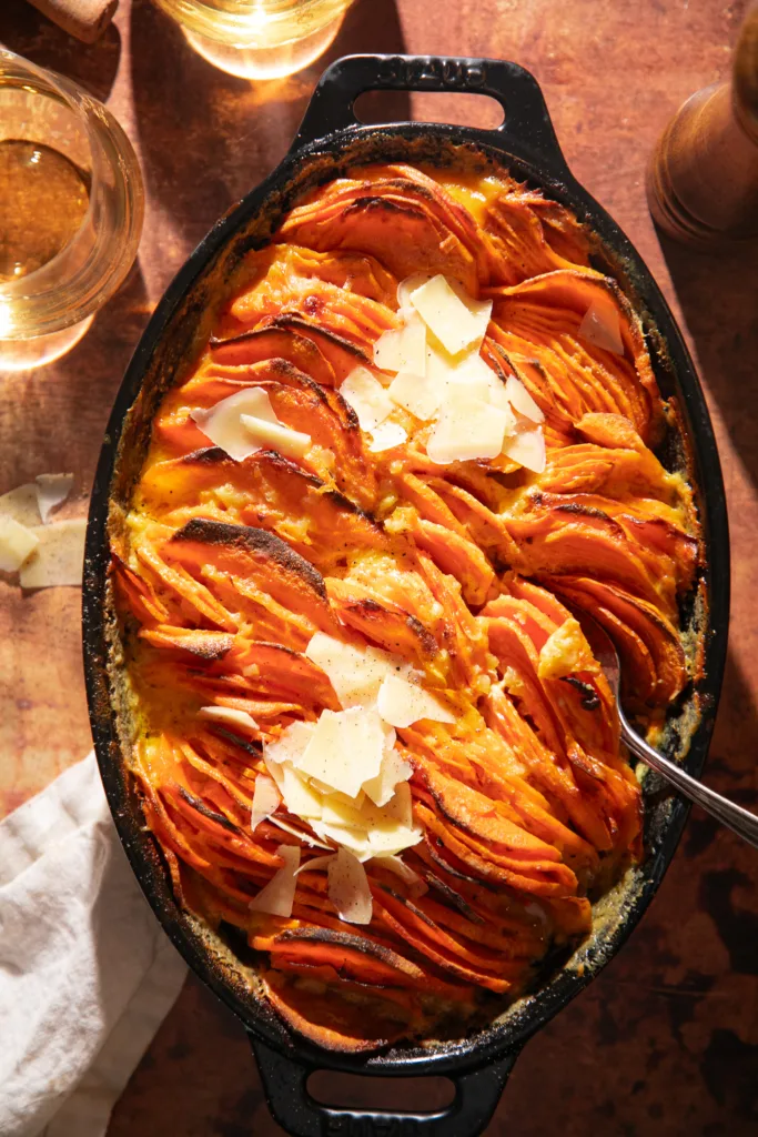 Close-up of golden baked sweet potato gratin with layers of thinly sliced sweet potatoes and melted parmesan in a cast iron dish.