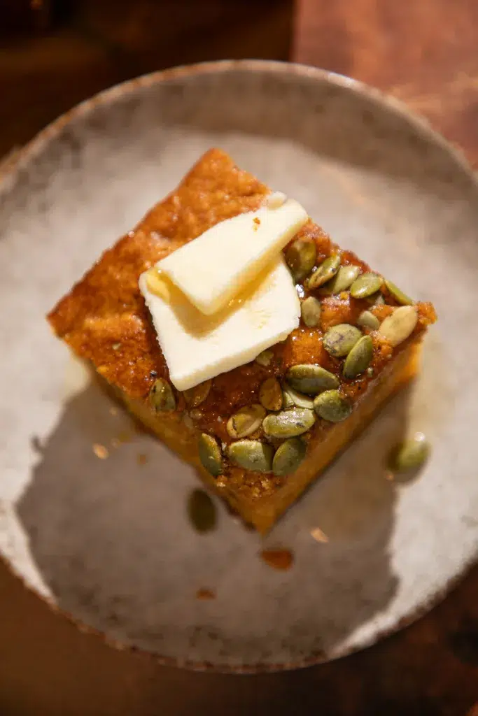 Close-up of a slice of maple pumpkin banana bread topped with butter and extra pepitas.