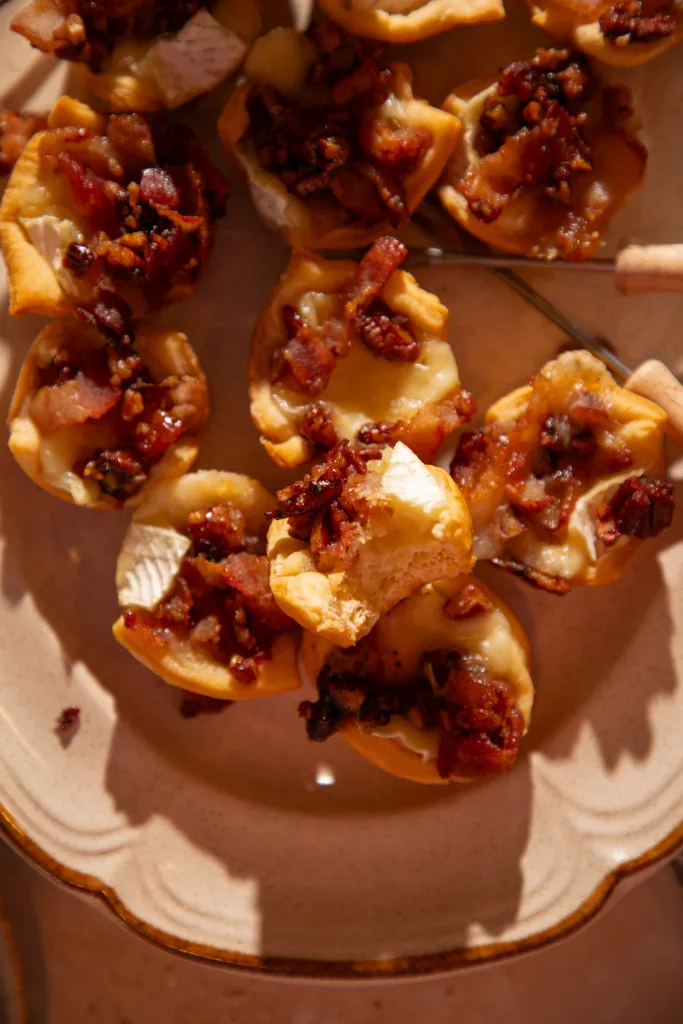 Warm maple bacon brie bites on a platter, one with a bite taken out showing melted cheese.