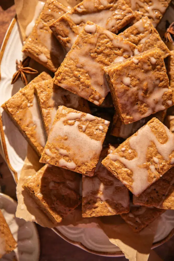 Overhead shot of gingerbread bars on a plate lined with parchment, drizzled with espresso glaze, styled with ribbons and a mug of coffee for a warm holiday setting.